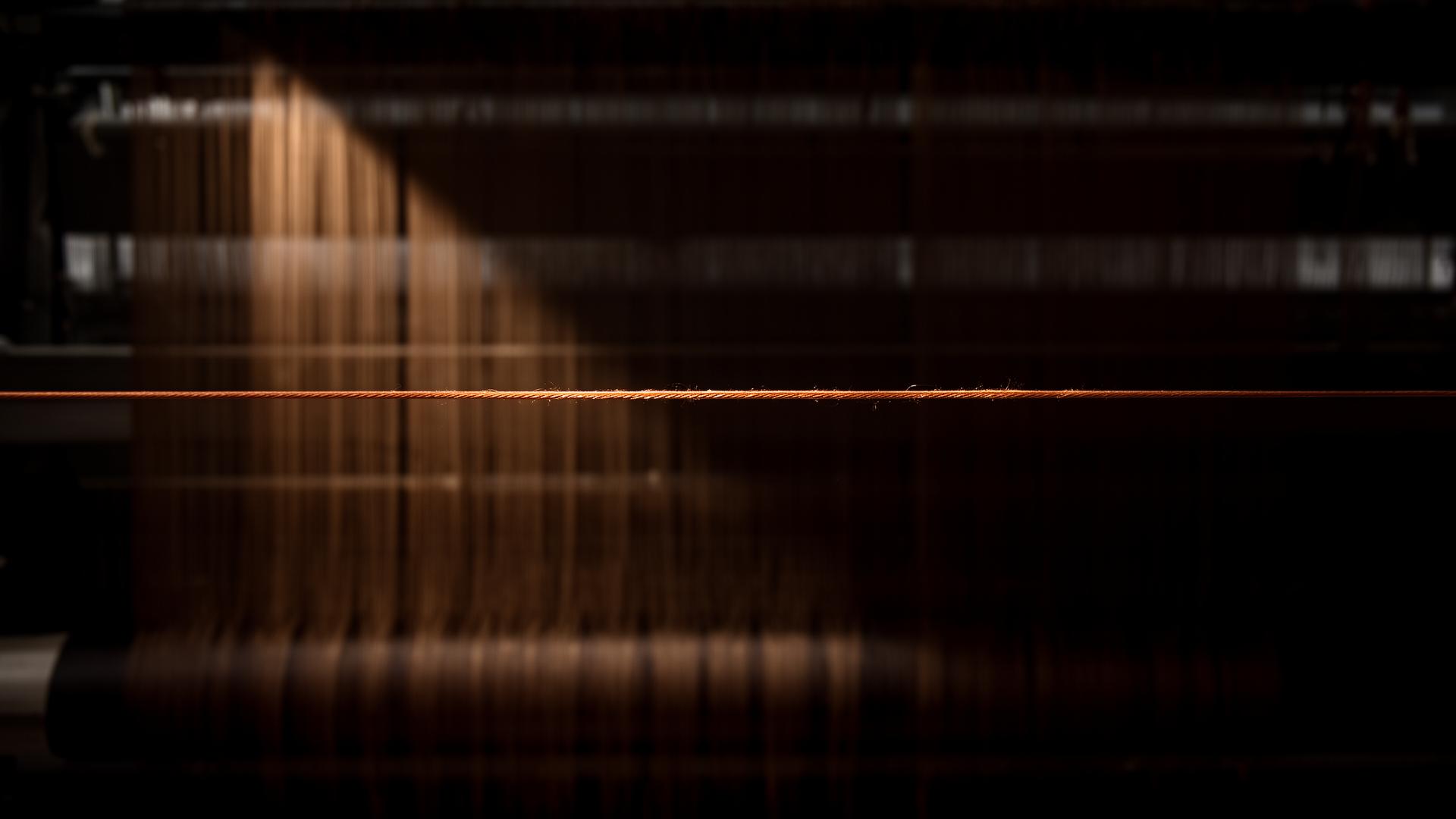 Single copper thread stretched across a Suzhou silk loom in deep shadow